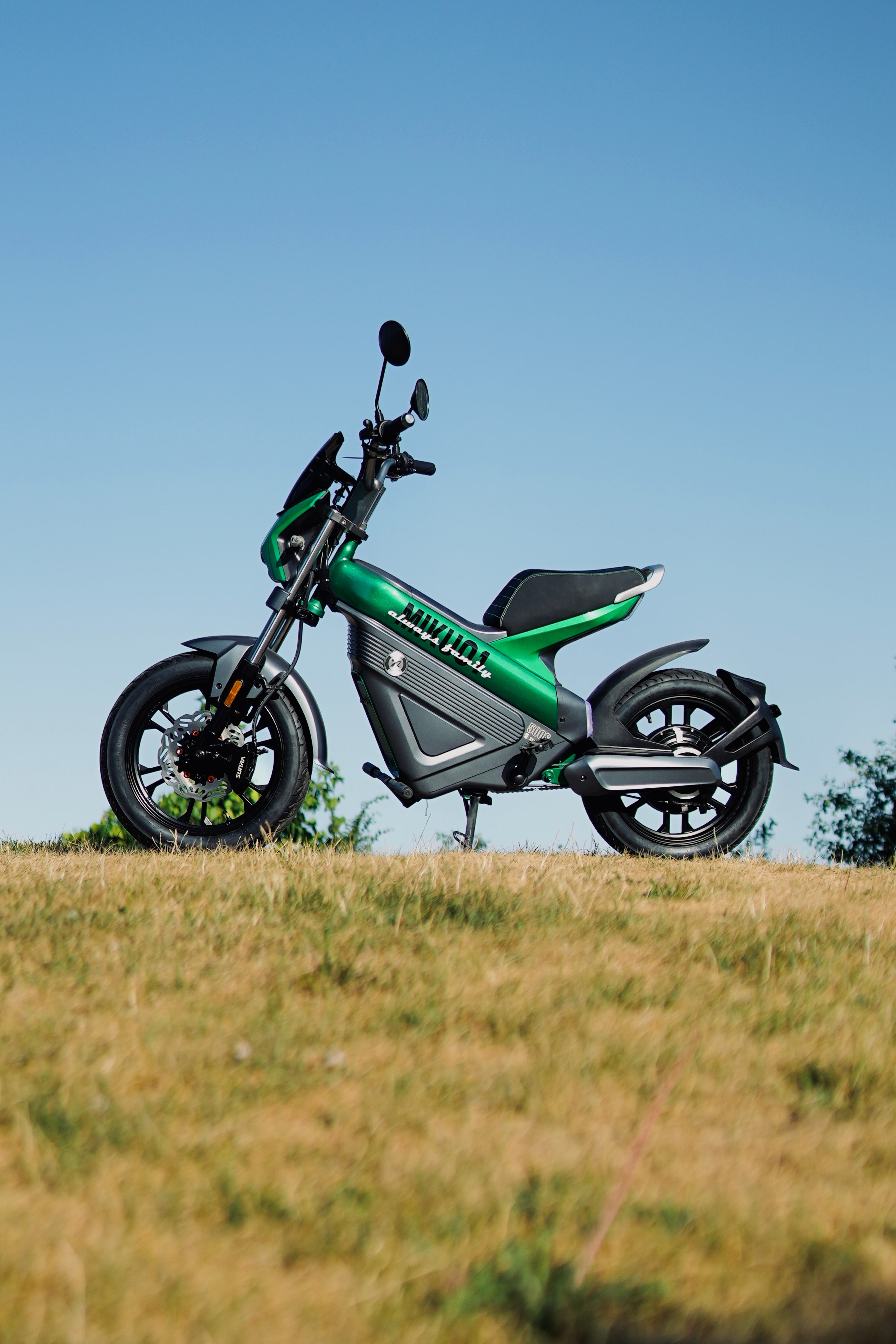 Green electric scooter on a grassy hill with a clear blue sky